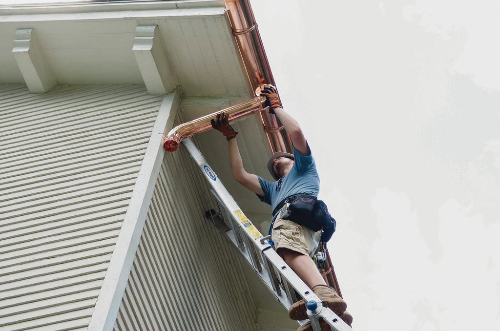 gutter contractor services - installation of copper gutters with tech on ladder