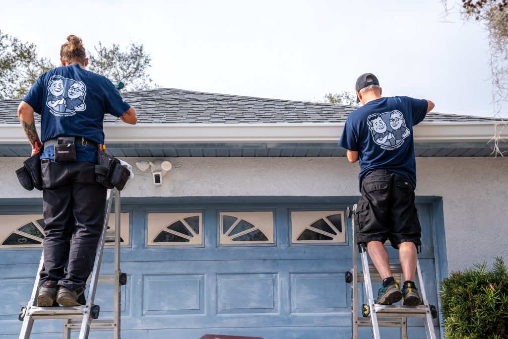 Two Brothers Gutters installers install a white gutter to the face of a house